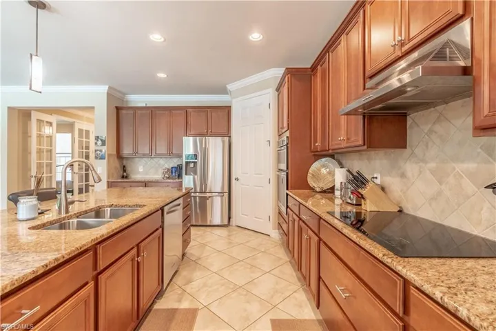 Kitchen featuring backsplash, light stone countertops, appliances with stainless steel finishes, sink, and ornamental molding