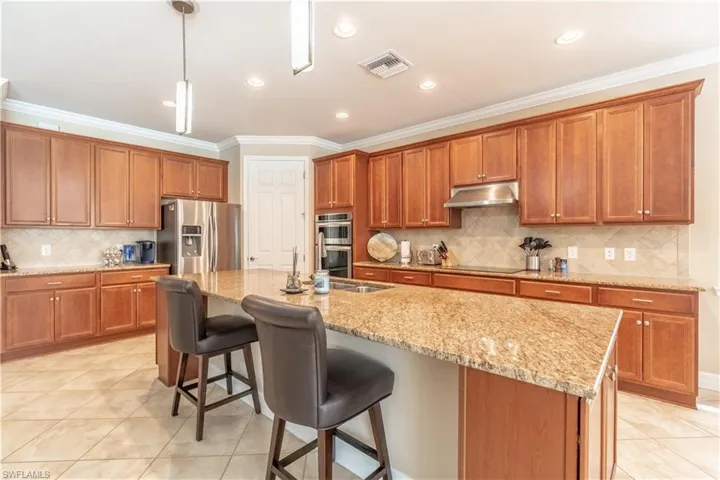 Kitchen with light tile patterned flooring, decorative backsplash, a kitchen island with sink, and stainless steel appliances