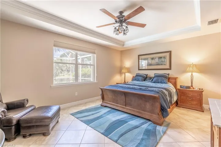 Bedroom with light tile patterned floors, ceiling fan, and a raised ceiling