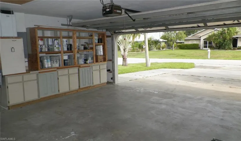 Garage interior featuring built-in wood cabinetry with open shelving and closed storage, a concrete floor, and a roll-up garage door mechanism