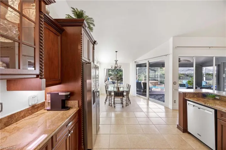 Kitchen with dishwashing machine, light tile patterned floors, vaulted ceiling, stainless steel fridge with ice dispenser, and decorative light fixtures