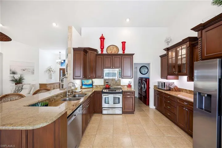 Kitchen with appliances with stainless steel finishes, a peninsula, light stone countertops, light tile patterned floors, and glass insert cabinets