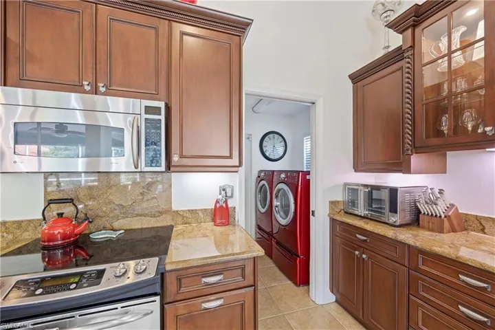 Kitchen featuring washer and dryer, stainless steel appliances, decorative backsplash, glass insert cabinets, and light tile patterned floors