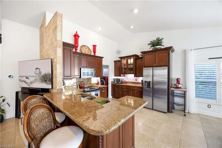 Kitchen with stainless steel appliances, a peninsula, light tile patterned floors, light stone countertops, and high vaulted ceiling