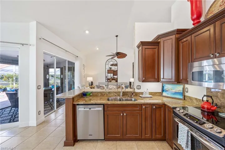 Kitchen with appliances with stainless steel finishes, a ceiling fan, a peninsula, light stone counters, and lofted ceiling