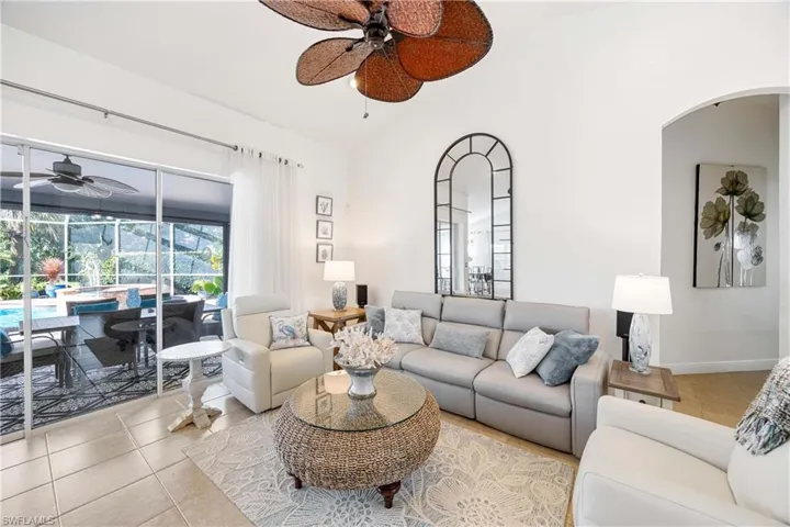 Tiled living room with a ceiling fan, a sunroom, arched walkways, and lofted ceiling