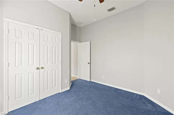 Unfurnished bedroom featuring dark carpet, a closet, and a ceiling fan