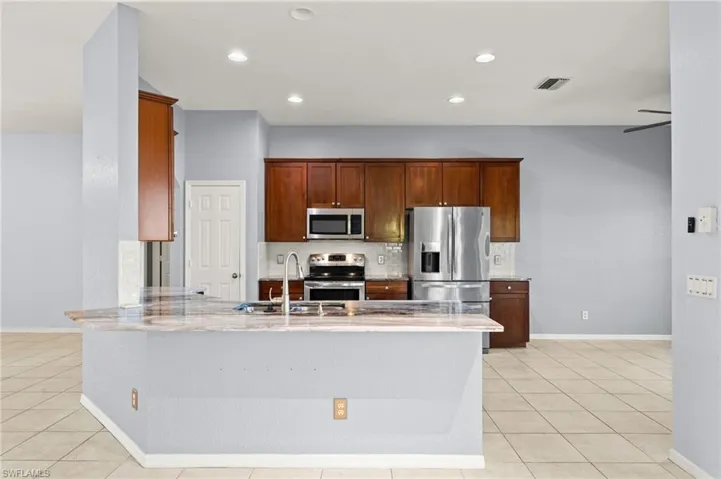 Kitchen with stainless steel appliances, a peninsula, light tile patterned flooring, decorative backsplash, and recessed lighting