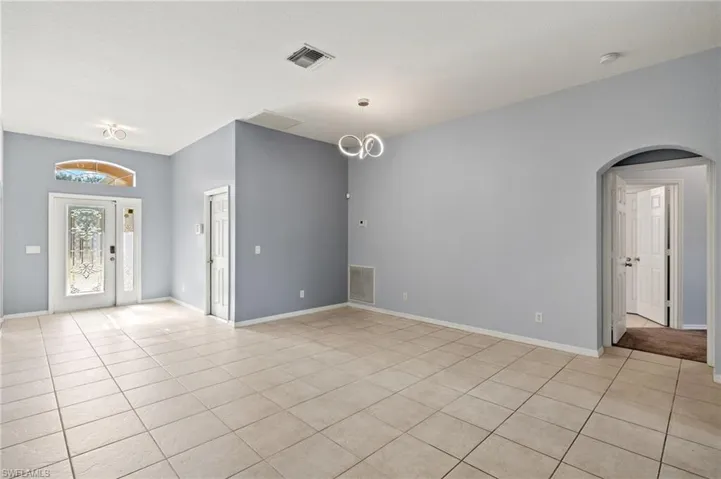 Empty room with light tile patterned flooring, arched walkways, a smoke detector, and a chandelier
