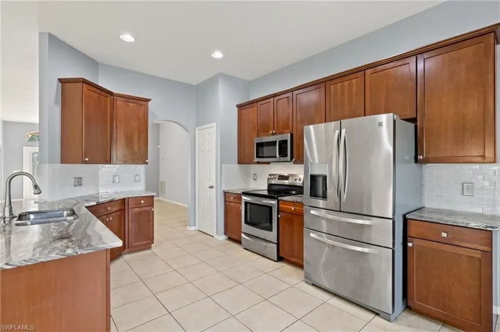 Kitchen with stainless steel appliances, tasteful backsplash, arched walkways, light stone countertops, and recessed lighting