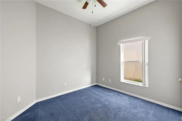 Empty room featuring a ceiling fan and dark colored carpet