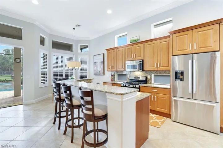 Kitchen featuring appliances with stainless steel finishes, crown molding, light stone counters, a center island, and backsplash
