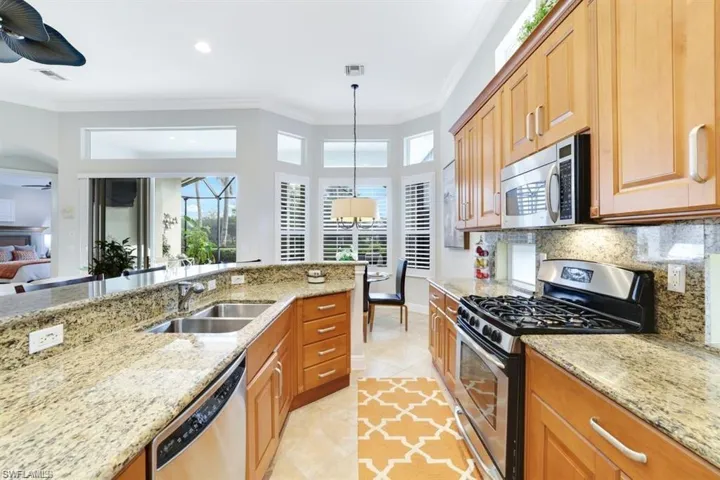 Kitchen with stainless steel appliances, crown molding, plenty of natural light, light stone countertops, and hanging light fixtures