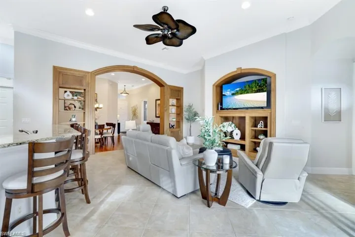 Living room with crown molding, arched walkways, light tile patterned floors, ceiling fan, and built in shelves
