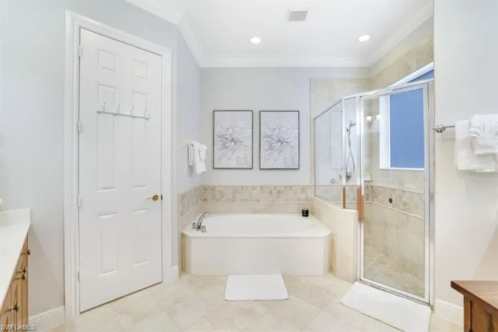 Full bathroom with vanity, a garden tub, a shower stall, crown molding, and light tile patterned floors