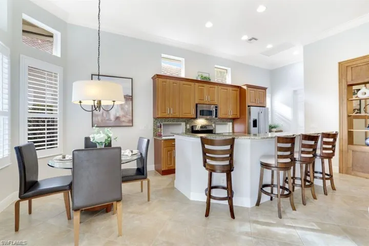 Kitchen with brown cabinetry, light stone countertops, ornamental molding, a breakfast bar, and tasteful backsplash