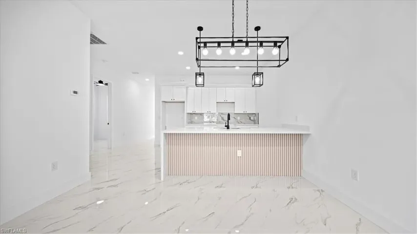 Kitchen featuring white cabinetry, a peninsula, a breakfast bar area, light stone counters, and light marble finish flooring