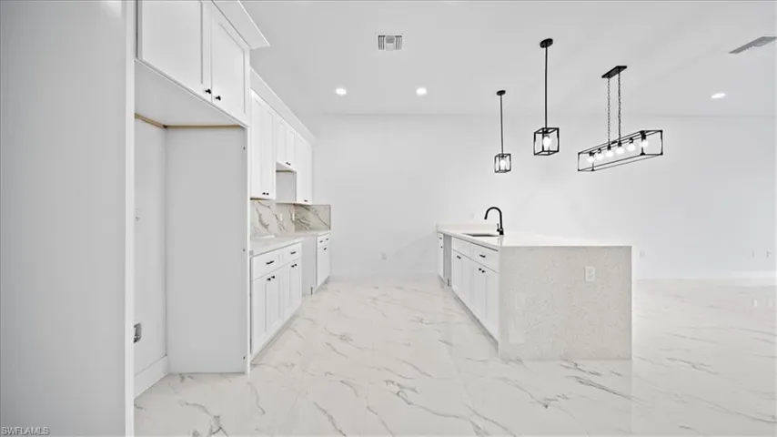 Kitchen featuring white cabinetry, light stone countertops, a peninsula, hanging light fixtures, and tasteful backsplash