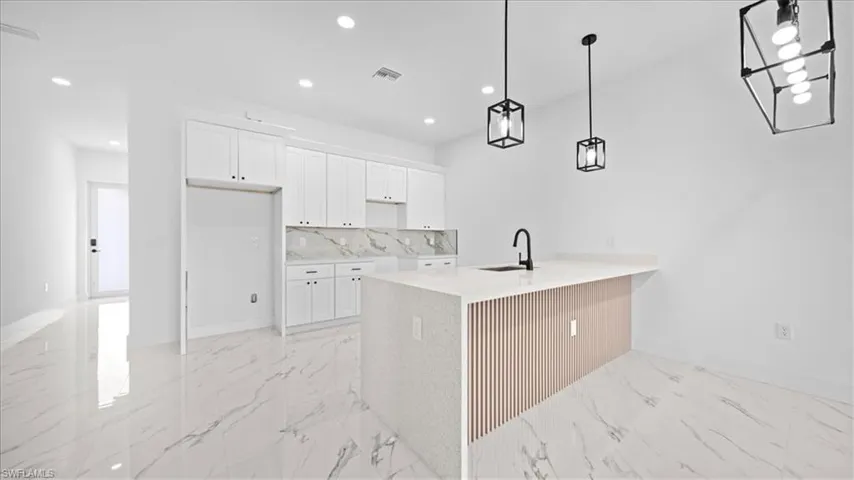 Kitchen featuring white cabinets, light stone counters, a peninsula, and light marble finish flooring