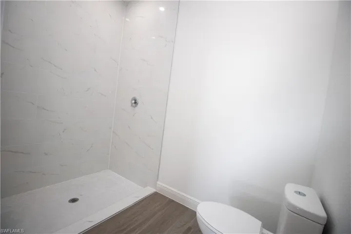Bathroom featuring vinyl-type flooring, toilet, and tiled shower