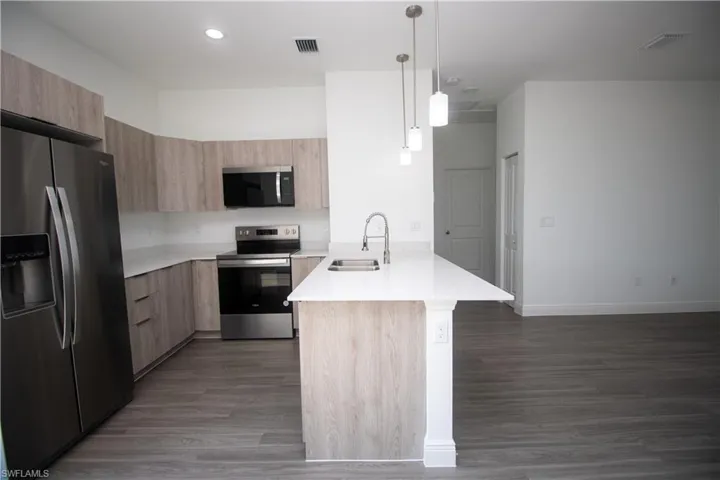 Kitchen featuring sink, light brown cabinets, appliances with stainless steel finishes, and hanging light fixtures
