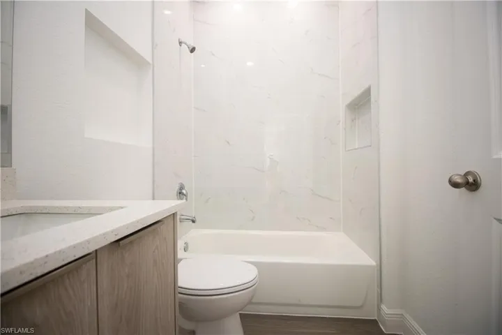Full bathroom with vinyl-style flooring, toilet, vanity, and tiled shower / bath