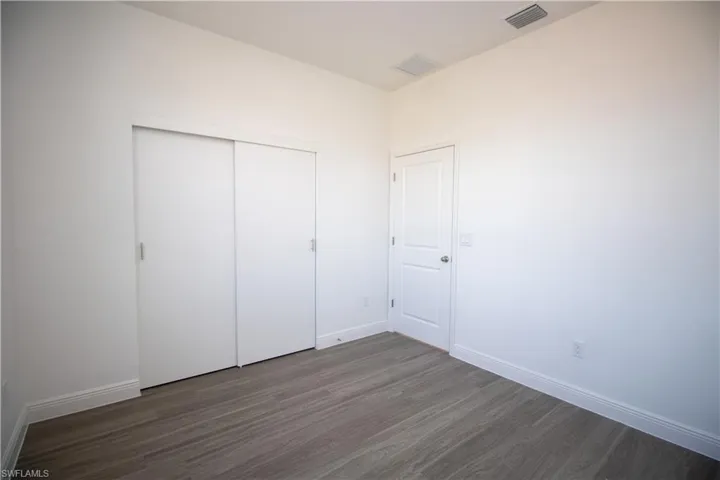 Bedroom with dark hardwood / wood-style floors and a closet