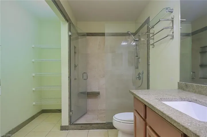 Bathroom with tile floors, a shower with door, vanity with extensive cabinet space, and toilet