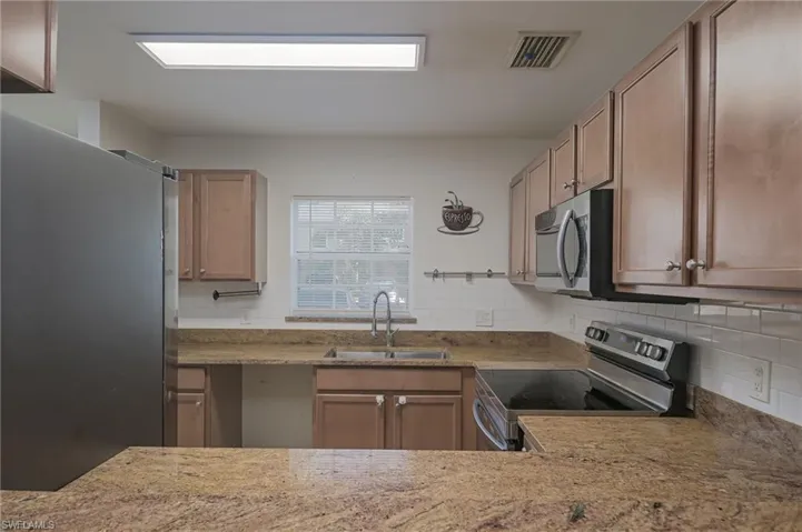 Kitchen featuring appliances with stainless steel finishes, sink, tasteful backsplash, and light stone countertops