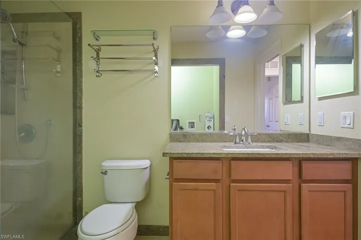 Bathroom featuring a shower with shower door, vanity with extensive cabinet space, and toilet