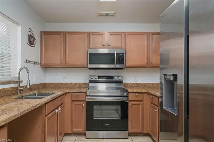 Kitchen with backsplash, light stone countertops, appliances with stainless steel finishes, sink, and light tile floors
