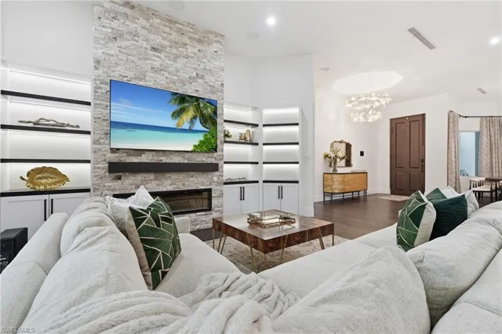 Stone-clad fireplace with a linear insert and built-in shelving, dark wood-finish flooring, and recessed lighting