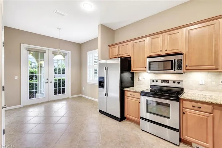 Kitchen featuring light tile patterned flooring, appliances with stainless steel finishes, decorative backsplash, light stone counters, and french doors