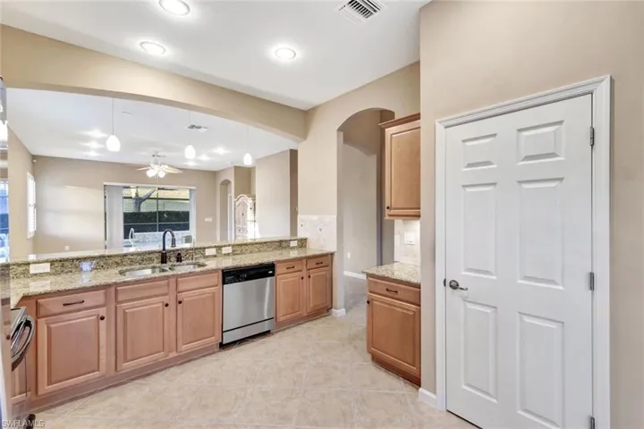 Kitchen with sink, range, stainless steel dishwasher, pendant lighting, and light stone countertops