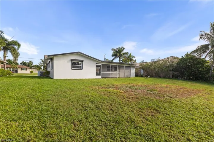 Rear view of property featuring a lawn, a sunroom, and stucco siding