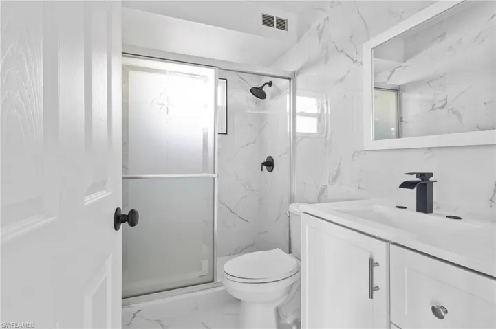 Bathroom featuring vanity, marble finish floors, a marble finish shower, and tile walls