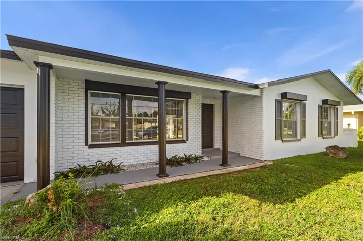 Property entrance with brick siding, a lawn, a porch, and an attached garage