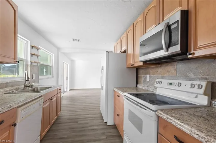 Kitchen with white appliances, backsplash, open shelves, dark wood-type flooring, and light stone countertops