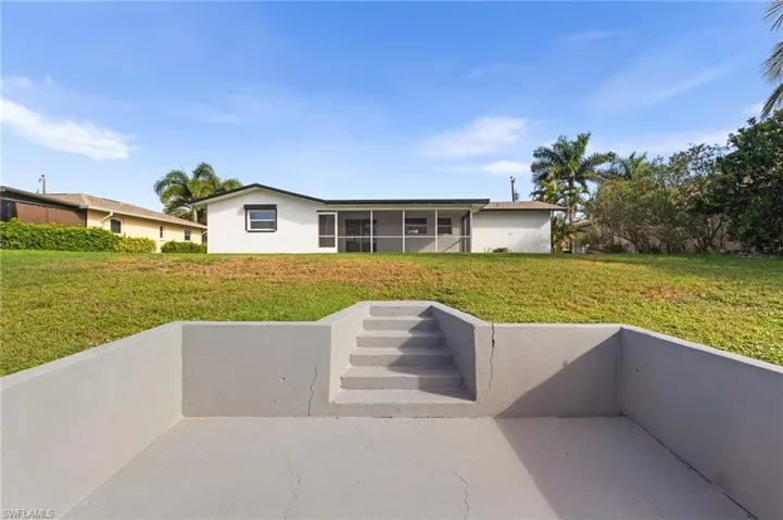 Rear view of house with a lawn, a sunroom, a patio area, and stucco siding
