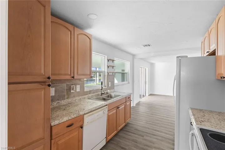 Kitchen featuring white appliances, dark wood-type flooring, decorative backsplash, light brown cabinets, and light stone countertops
