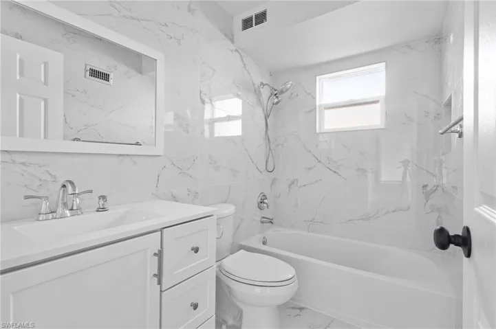 Bathroom featuring shower / washtub combination, vanity, marble finish flooring, and tile walls