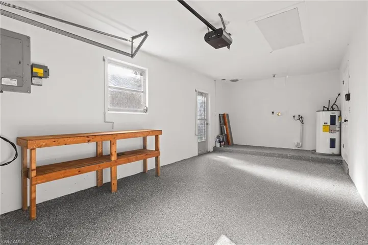 Garage featuring electric panel, electric water heater, and a garage door opener