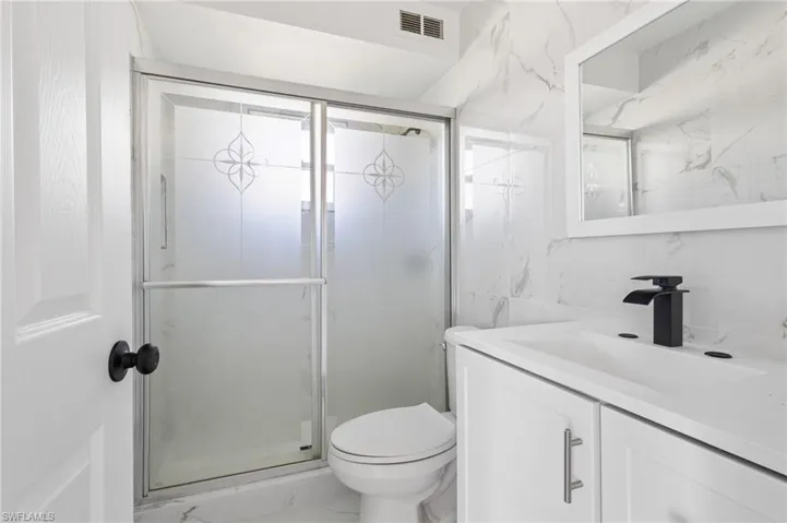 Bathroom with vanity, a stall shower, tile walls, and light marble finish flooring