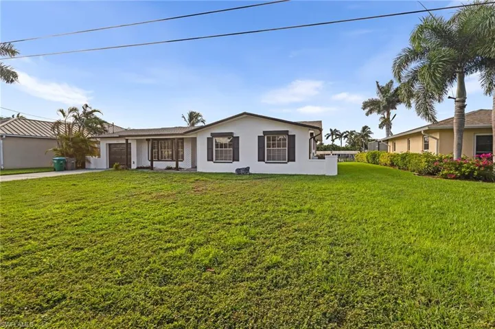 Ranch-style home with a front yard, a garage, stucco siding, and driveway