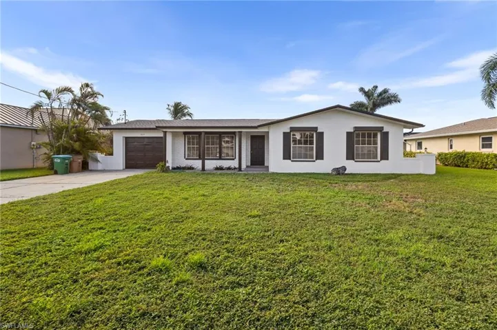 Single story home featuring driveway, a garage, a front yard, and stucco siding