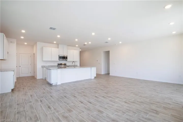 Kitchen with white cabinetry, recessed lighting, open floor plan, wood finish floors, and stainless steel appliances