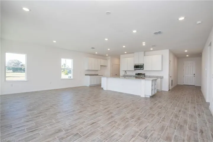 Kitchen with wood tiled floors, white cabinetry, an island with sink, open floor plan, and stainless steel appliances