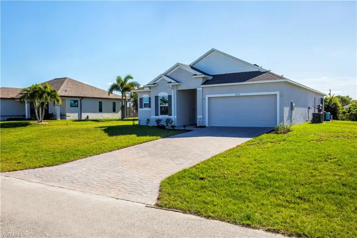 Ranch-style house featuring a front yard, decorative driveway, a garage, stucco siding, and roof with shingles