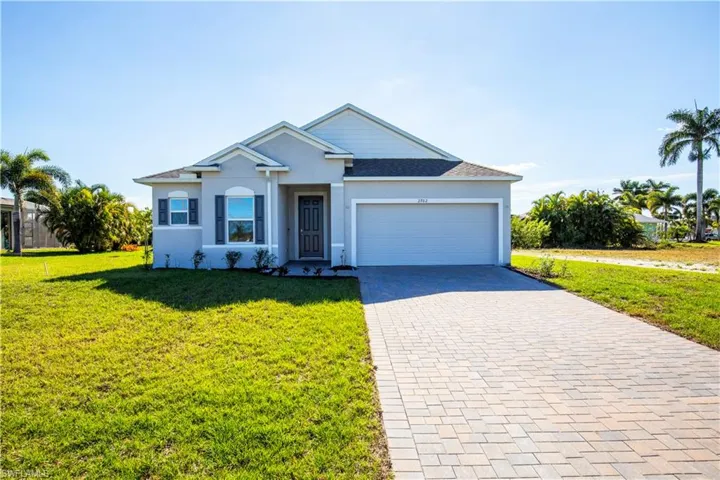 View of front facade featuring a front lawn, decorative driveway, a garage, and stucco siding