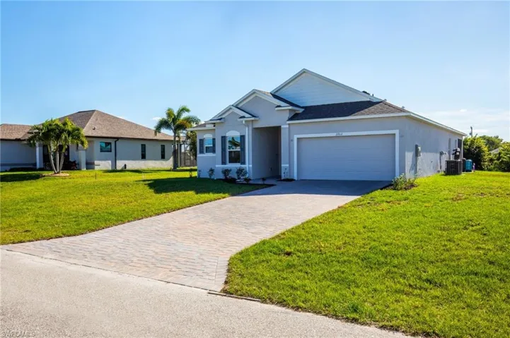 View of front of house featuring a front lawn, decorative driveway, stucco siding, and an attached garage